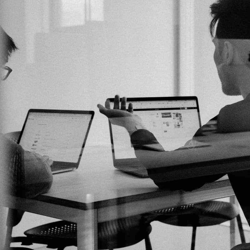 two individuals collaborating at a desk with laptops